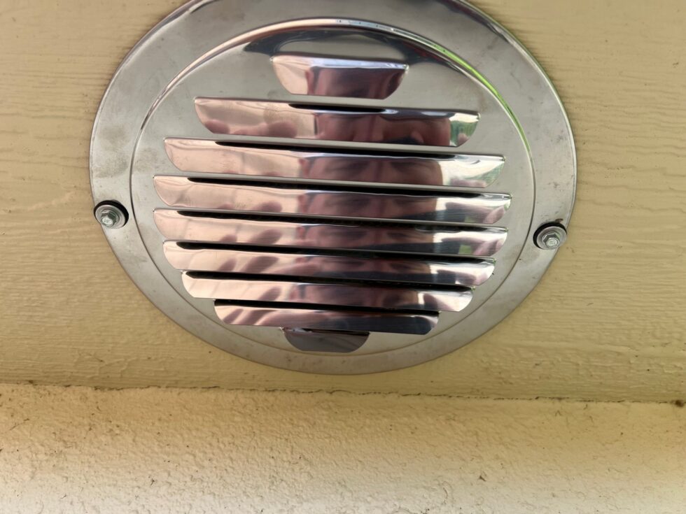A louvered chrome vent installed on the building's soffits as part of this unusual solar attic fan installation 